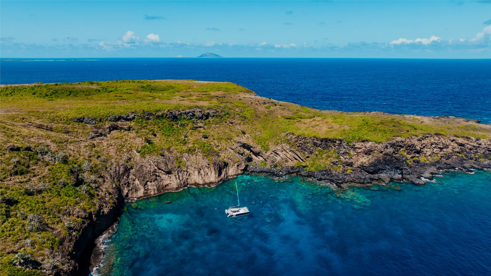 A small sailboat below a rocky green island.