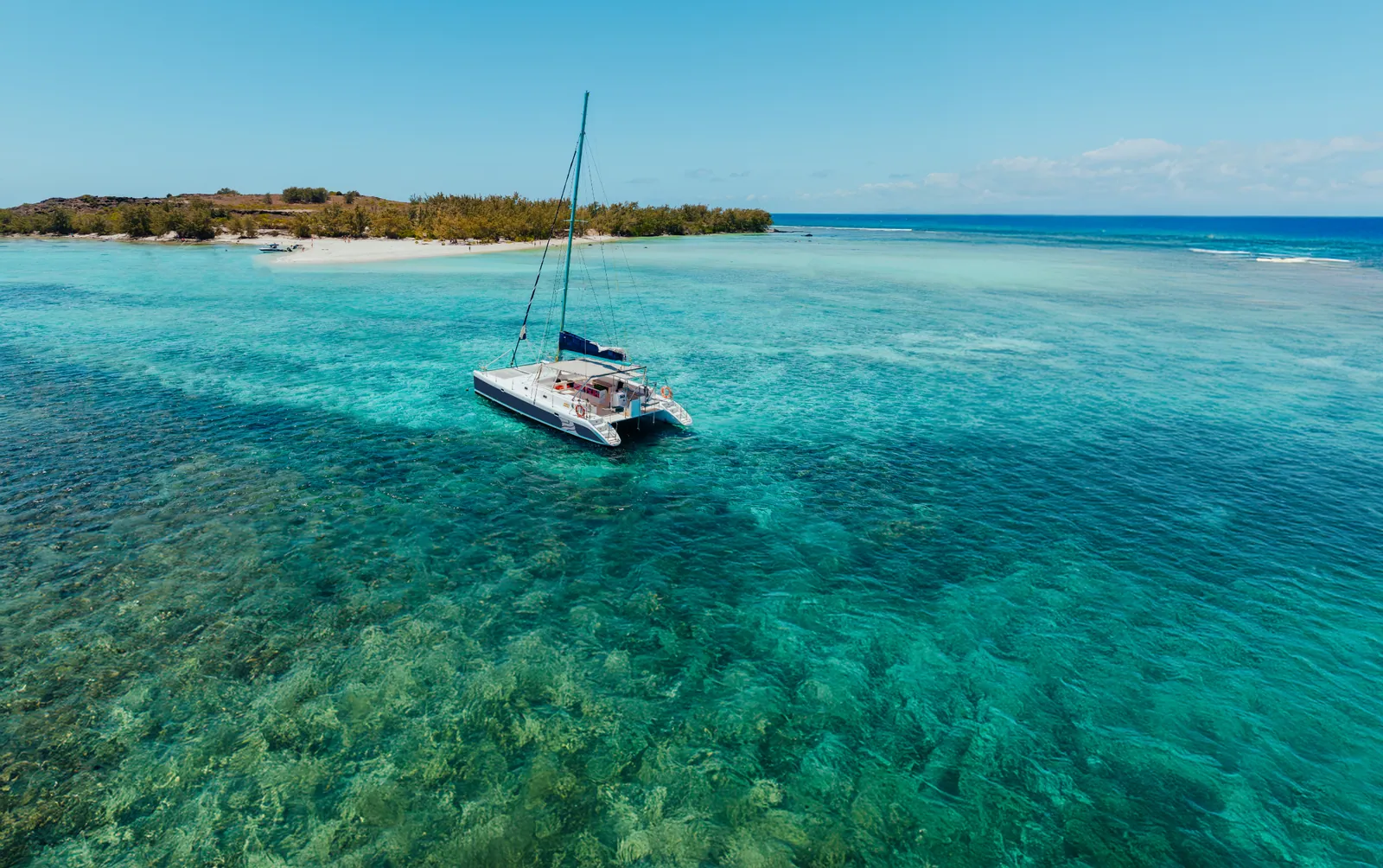 Aerial view of a catamaran anchored over shallow turquoise water.