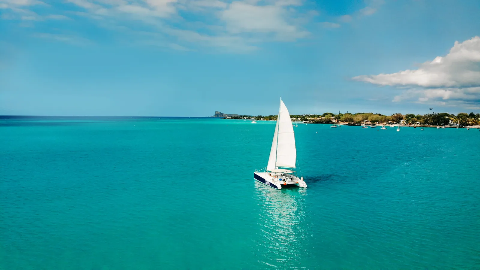 A white-sailed catamaran on a turquoise lagoon.