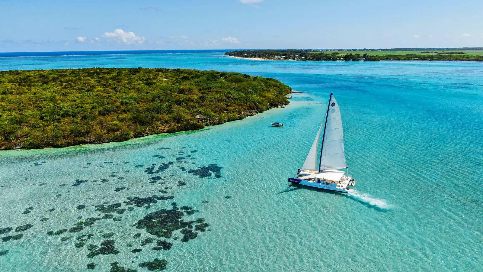 A catamaran sailing through a turquoise lagoon beside a green island.
