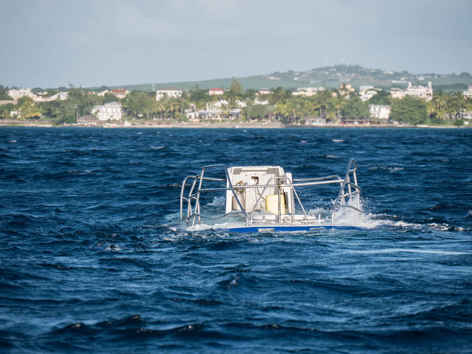 A partially surfaced submarine with the coastline behind it.