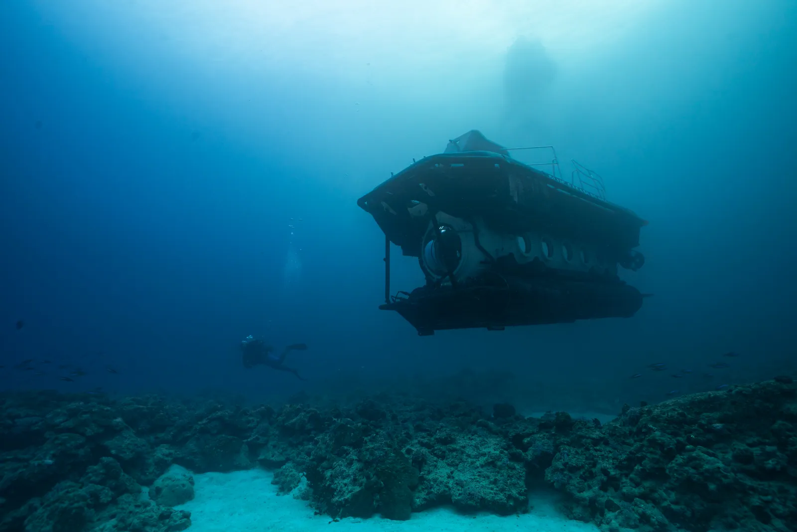 A submarine moving above the seabed in blue water.
